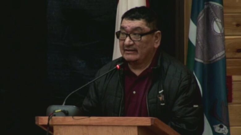 A man at a podium speaks to an audience of about forty people at an inquiry in Labrador examining the treatment of Innu children by the child protection system.