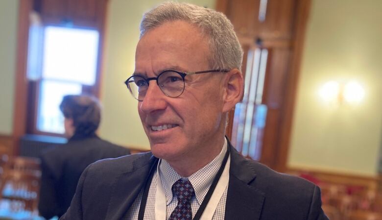 Head and shoulders picture of a grey-haired man wearing glasses and an indentification lanyard. 