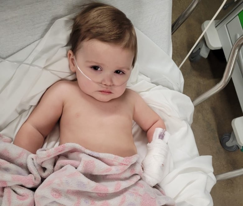 A small child lies on a bed breathing from an oxygen tube.