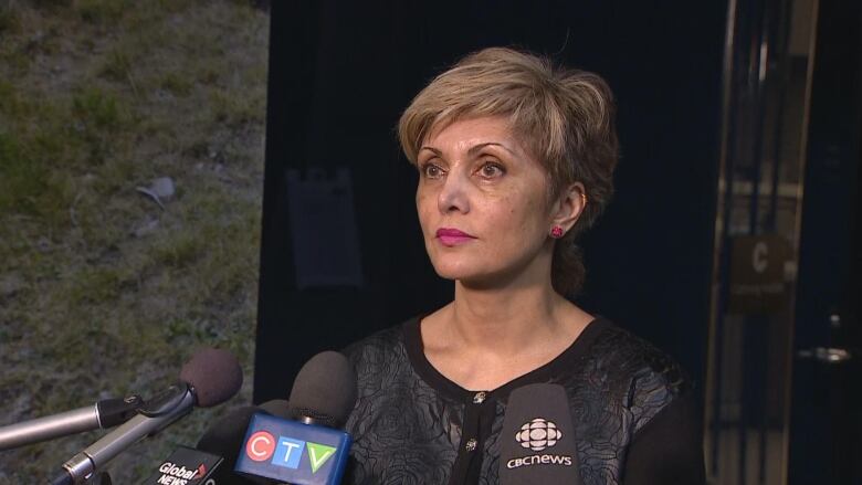 A woman stands in front of a line of microphones.