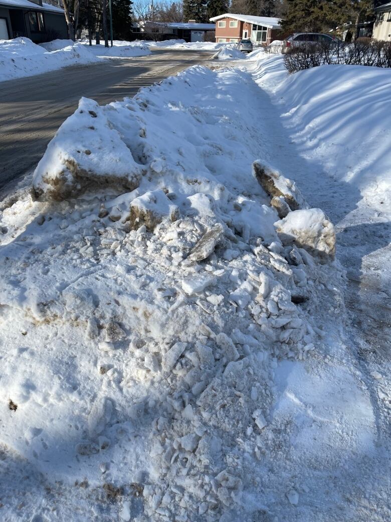 A pile of snow and ice towers above a snowy sidewalk.