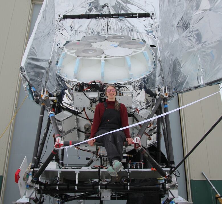 A woman sits in front of a large telescope.