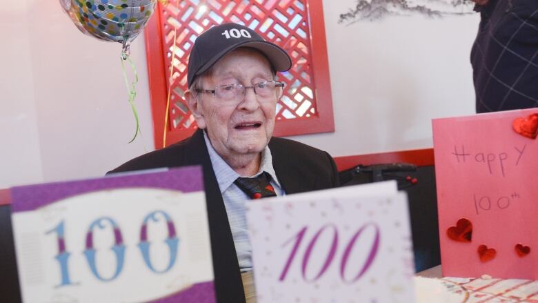 man sits behind greeting cards with 100 years written on them 