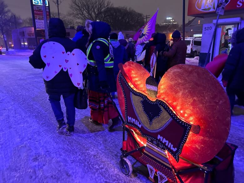 People on a snow-covered street pull a wagon with a red heart containing an image of a woman holding an MMIW blanket.