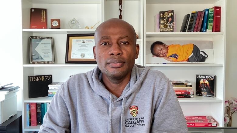 A man wearing a University of Calgary hoodie sits in an office.