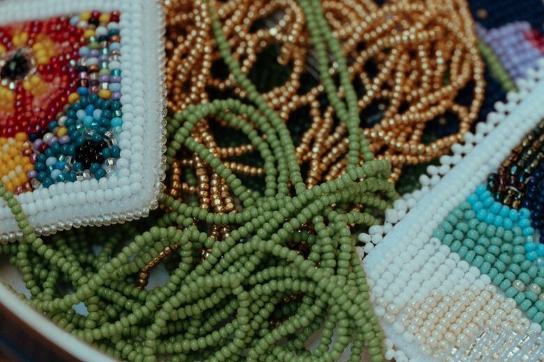 A pile of coloured beads with some pieces of beadwork resting on top of them.