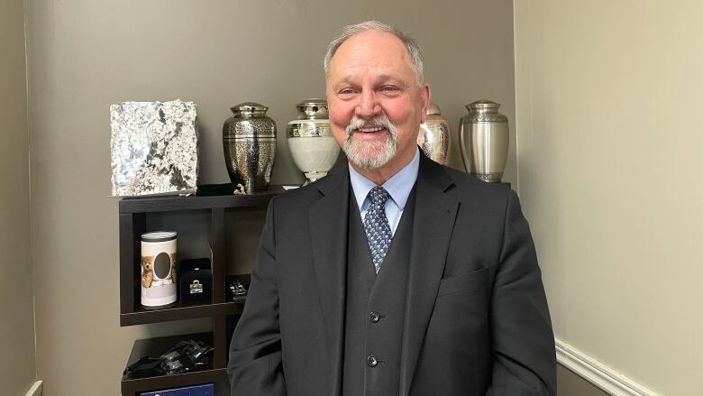 Collin Bourgeois stands in front of a shelf full of brass urns.