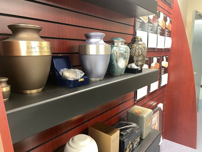 Colourful urns sit atop a wooden shelf in a funeral home.