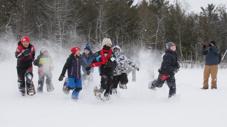 A group of kids frolic in the snow wearing snow shoes. 