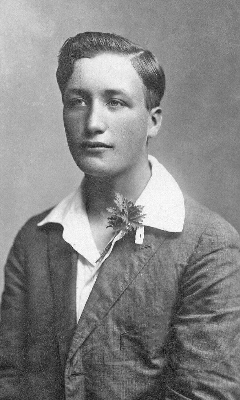 An old black and white photographic portrait of a young man, a boutonniere pinned to the collar of his white shirt.