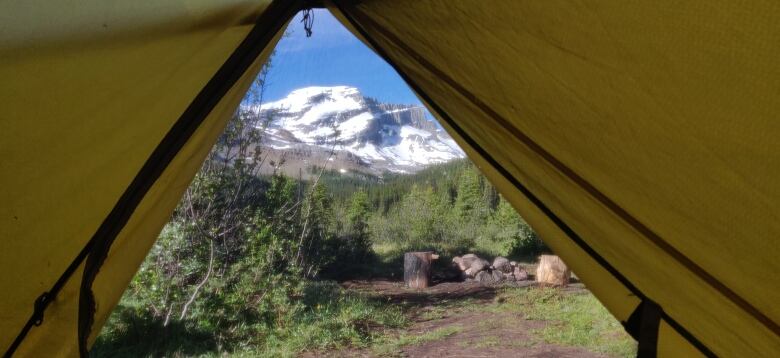 A snow-capped mountain is lit by the morning sun, seen through the mosquito netting and framed by the yellow flaps of a tent.