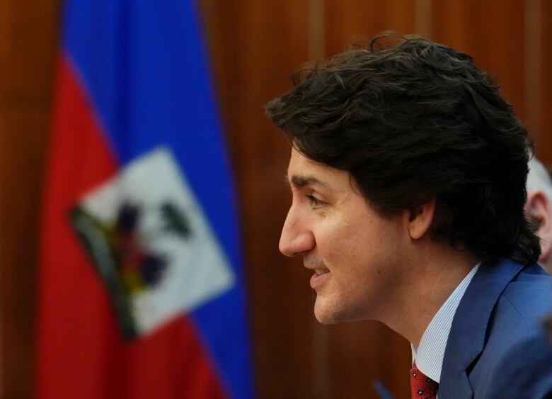 Prime Minister Trudeau sits in front of a Haitian flag.