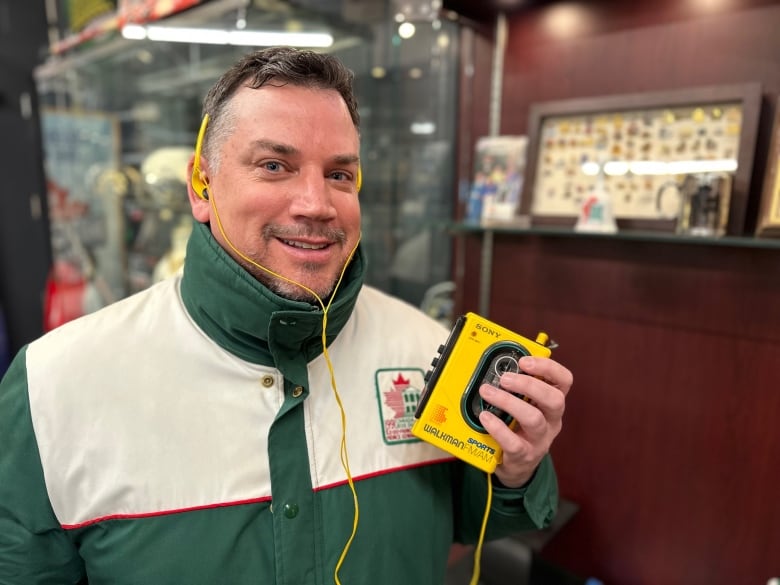 A man in a green and white jacket holds a bright yellow Walkman music player 