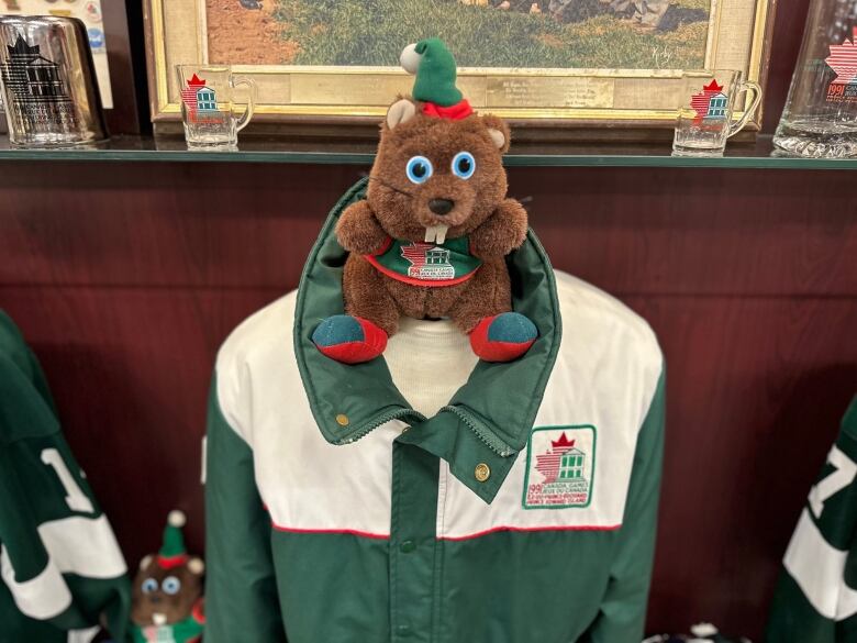 A small beaver plush toy sits above a green and white Canada Games jacket 