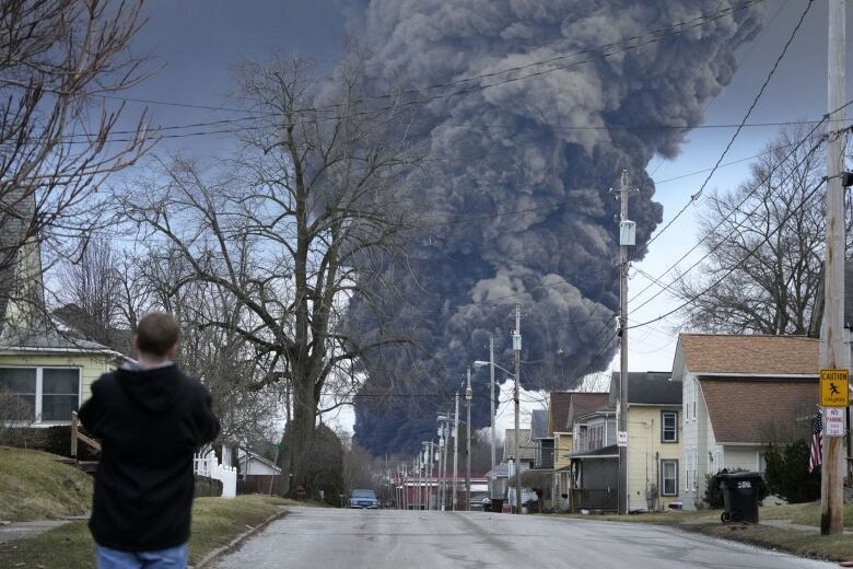 A person looks up at a giant cloud of smoke looming over a small town.