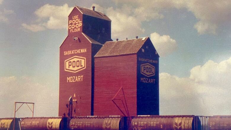 A 1970s style photograph of a tall, red grain elevator in front of a train