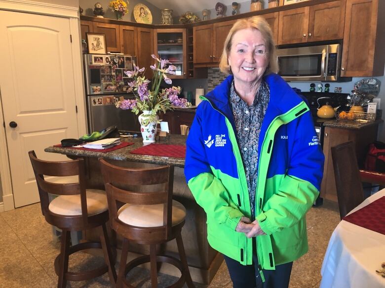 A woman wearing a Canada Games 2023 jacket smiles at the camera in a kitchen.