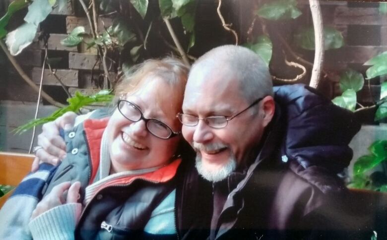 A man and woman smile sitting on a bench with leaves cascading behind them.