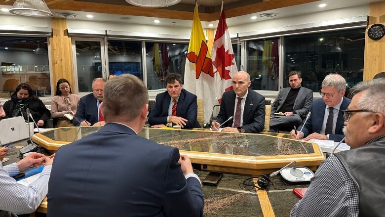 Men in suits at a table, Nunavut flag. 