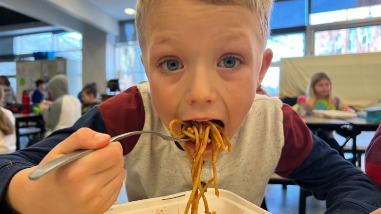 A young boy eats spaghetti with his mouth wide open