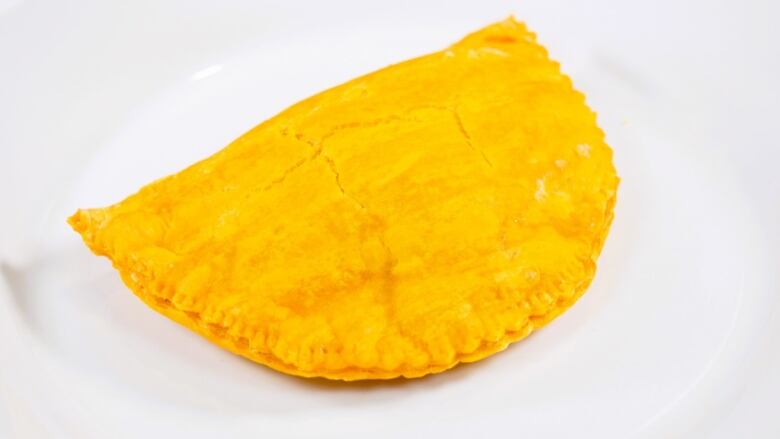 A tasty, flaky Jamaican patty sits on top of a white plate.