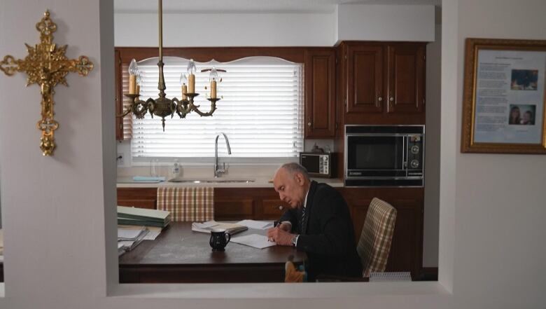 man sits at his dining room table with stacks of papers and files surrounding him