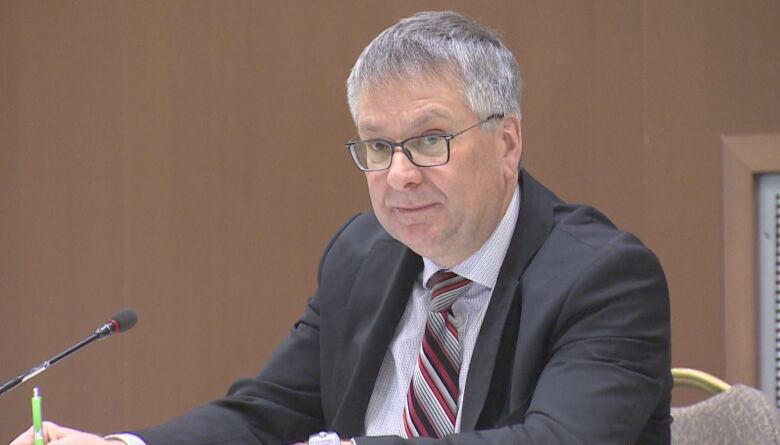 A man in a suit and tie and glasses writing in a notebook.