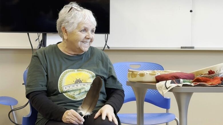 An Indigenous woman sits in a chair holding a feather.