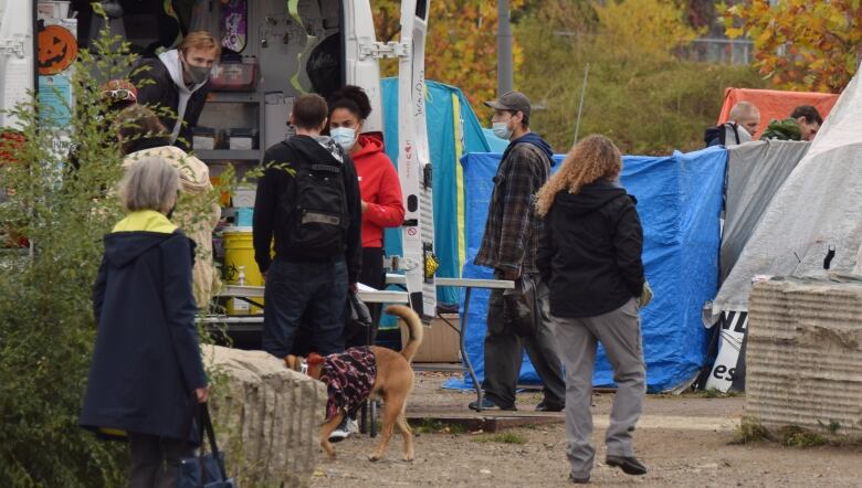 Van with open back door, workers wearing masks speak to people who are nearby.