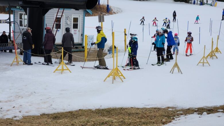 Skiers are seen on snow with grassy patches.