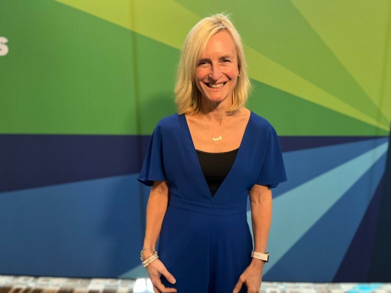 woman stands in front of green and blue backdrop, smiling at the camera.