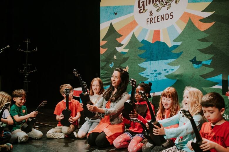 A woman sits with a bunch of children on the ground looking at violins.