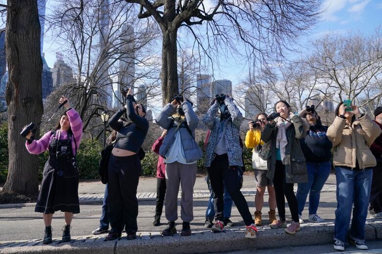 A small crowd of young people use binoculars to get a better look at an owl that is out of frame.