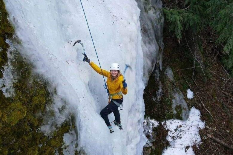 A woman in a yellow coat and white helmet is seen ice climbing.