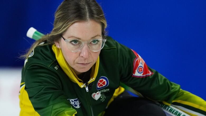 A female curler slides a rock along the ice.