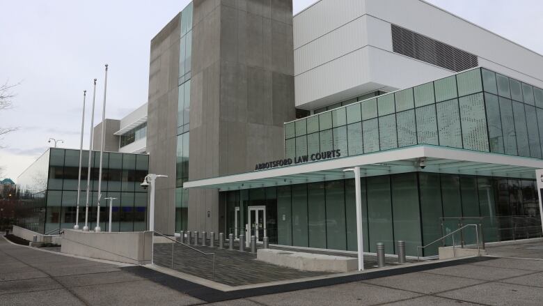 A building that appears to be outfitted with a facade of glass and cement is pictured. A simple text signage 'Abbotsford Law Courts' is installed in front.