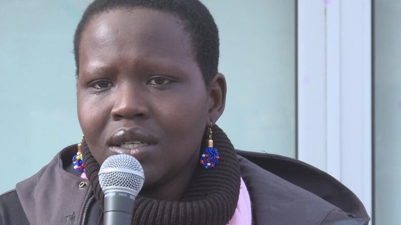 A woman speaks into a microphone, she is wearing a black scarf