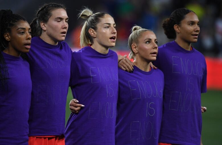 A group of female soccer players stand side by side while wearing T-shirts that read 'enough is enough'.