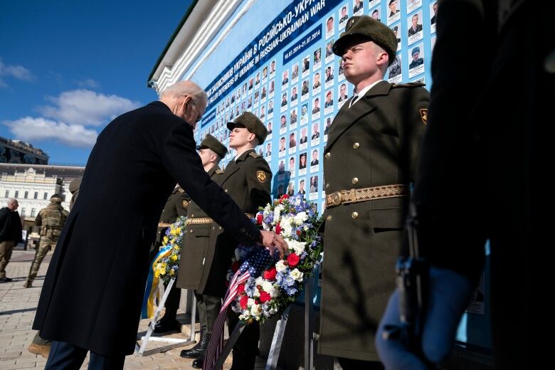 A man lays a wreath at a memorial while soldiers stand guard.