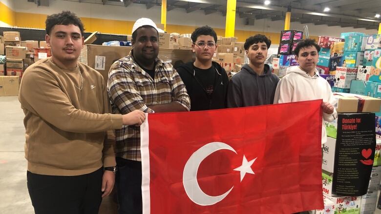 A group of people are standing holding the flag of Turkey in a warehouse.