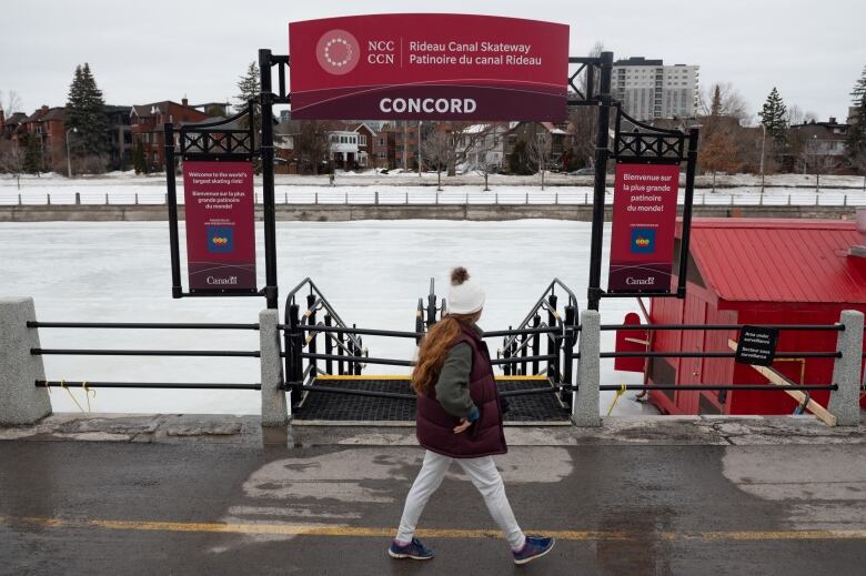 Someone walks beside a closed gate to a frozen waterway.