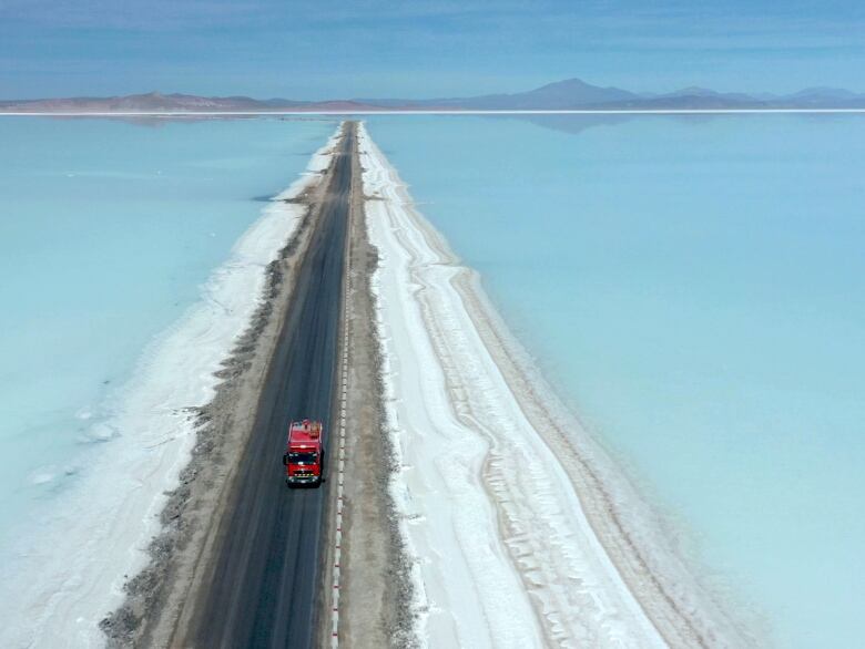 Red truck drives on a road between two expansive lithium pools.