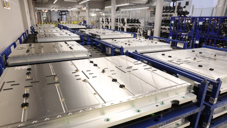 Rows of large, rectangular metal-encased batteries sit on shelves in a factory.