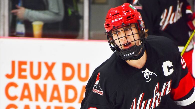 A teenager with long hair dressed in hockey gear inside a hockey rink.