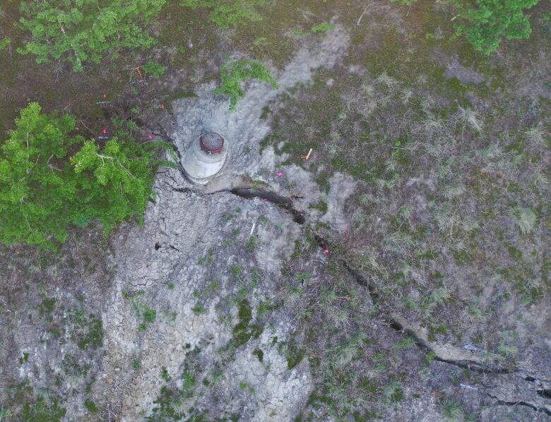 An overhead view of a manhole on a treed slope, with a large crack in the soil.