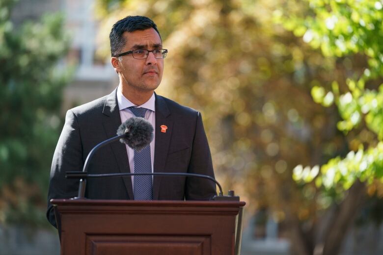 A man in a suit speaks at a podium at an outdoor event.