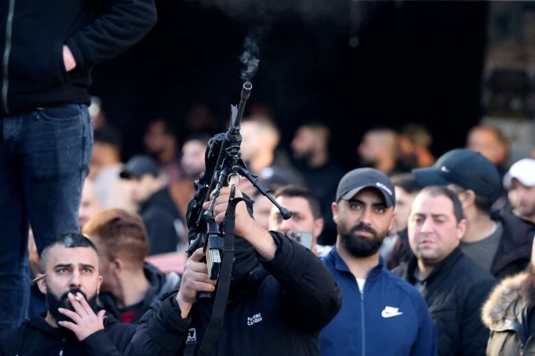 A man fires a rifle in the air as others look on.