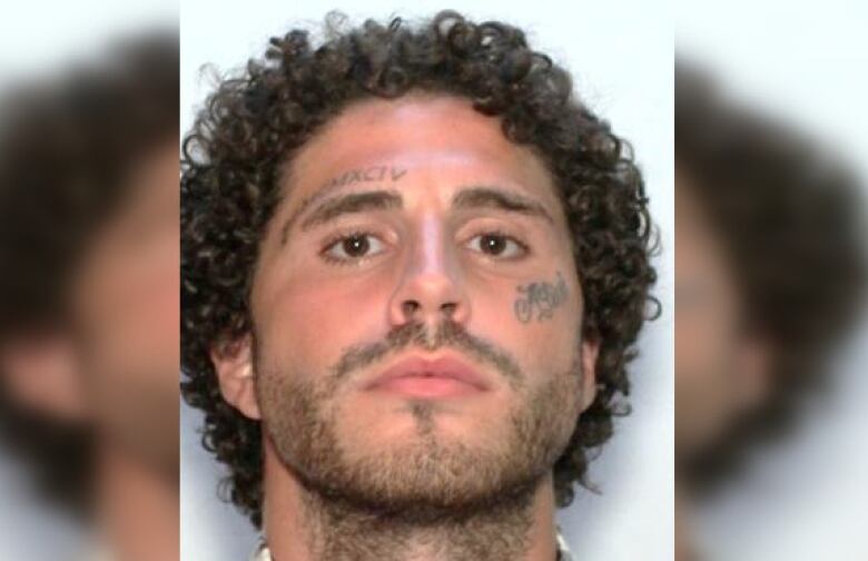 A mug shot of a man with curly hair and face tattoos