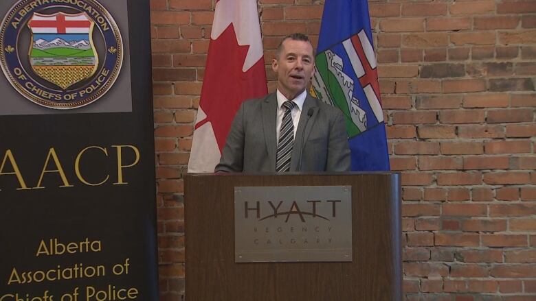 A man in a grey suit speaks at a podium that has a Hyatt hotel logo on it.