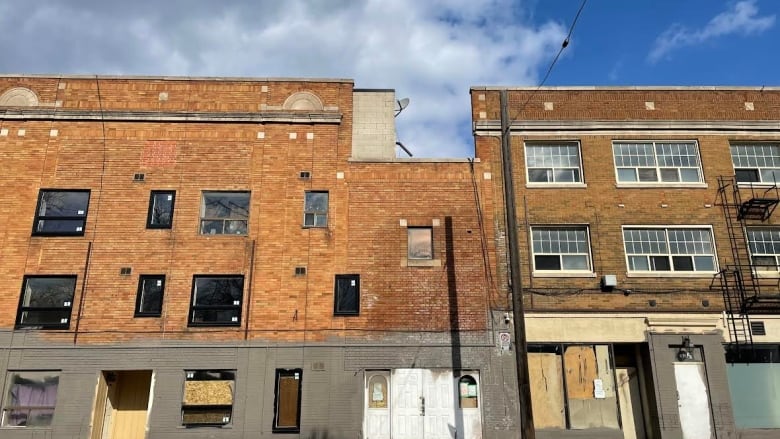 A three story brick building with new and boarded up windows.